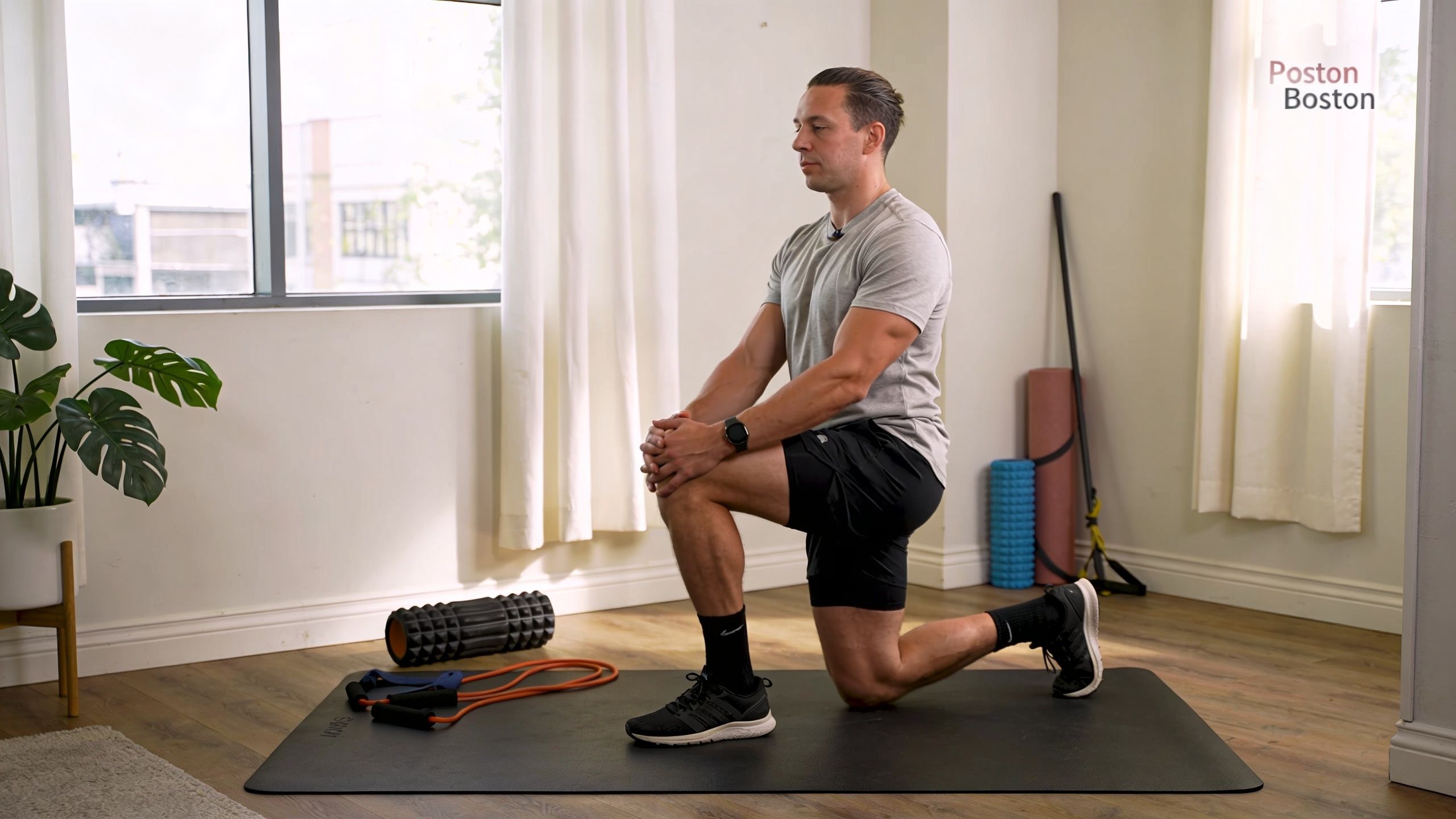 A man performing a kneeling hip flexor stretch on a yoga mat in a bright studio.