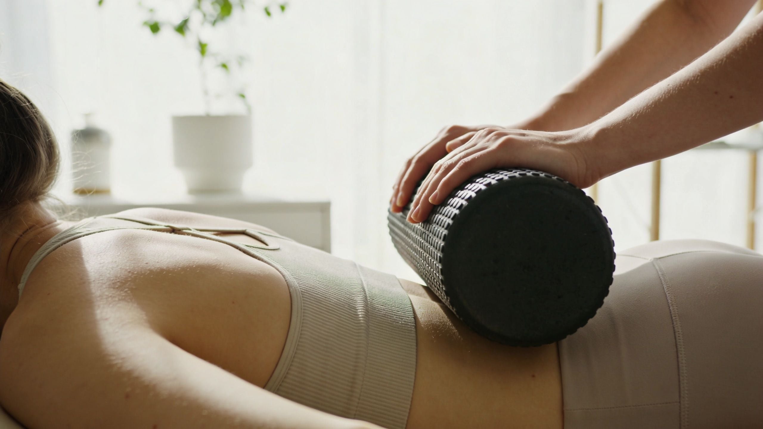 A physical therapist uses a foam roller on a patient's lower back during a wellness session.
