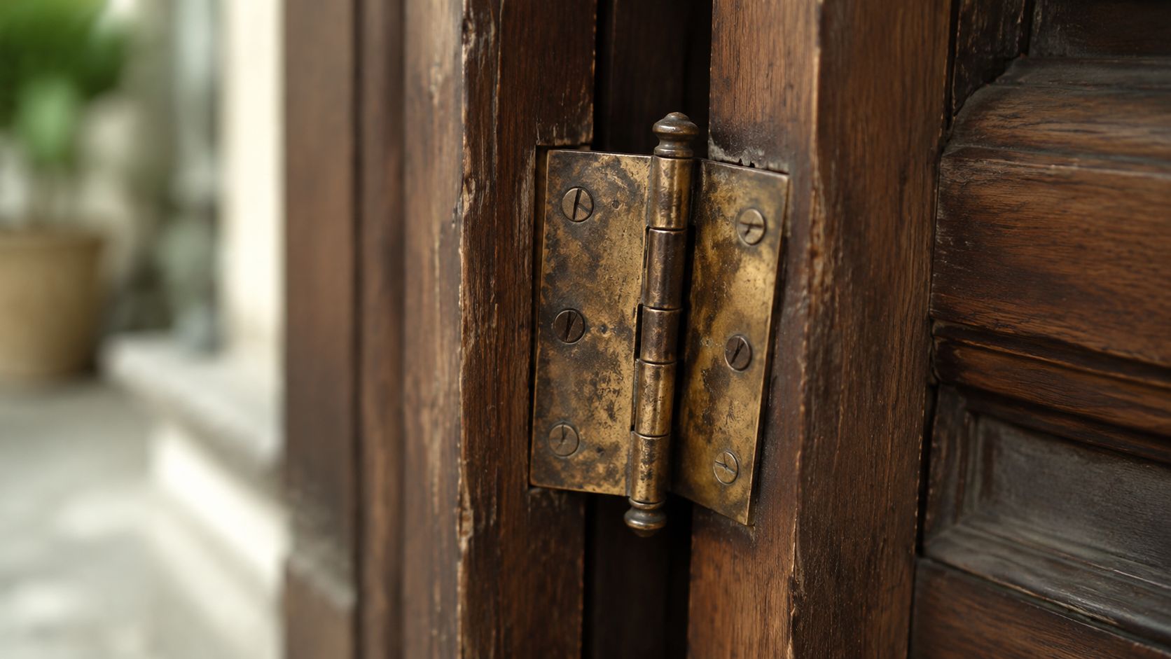 A close-up view of an antique metal door hinge attached to a weathered wooden door frame.